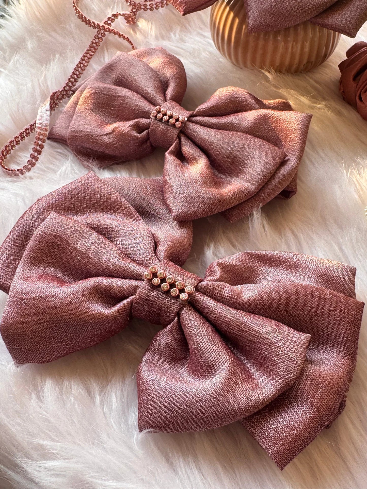 Two rose gold silk hair bows with pearl stone detailing, handmade by Bows and Bags India, displayed on white fur styling