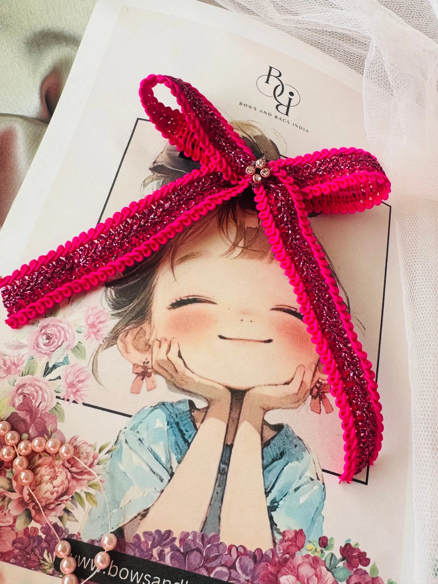 Magenta sequined hair bow with purple and gold detailing on illustrated lifestyle packaging, Bows and Bags India handmade