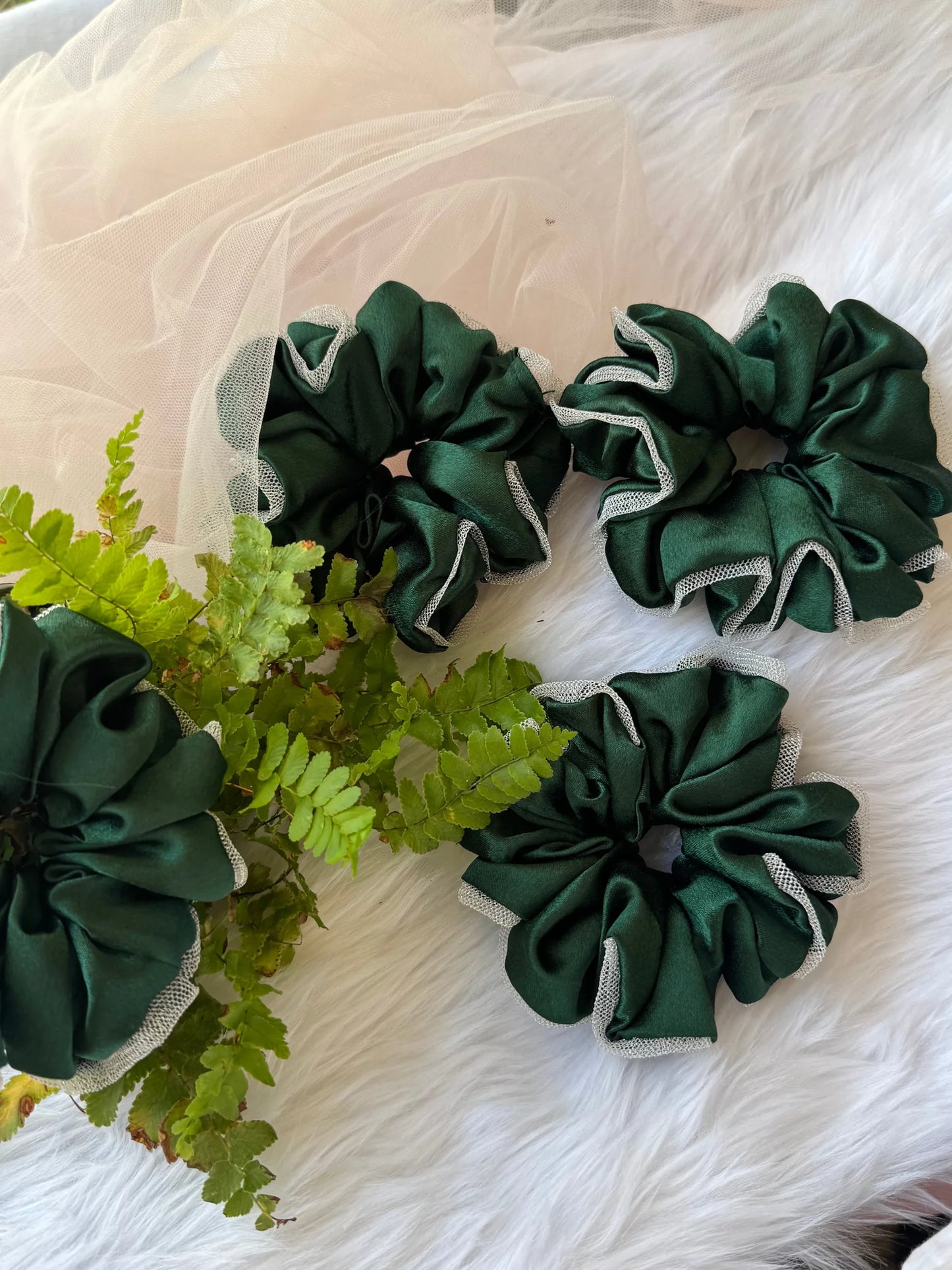 Dark green satin scrunchies with silver net borders displayed on white fur, handmade hair accessories by Bows and Bags India