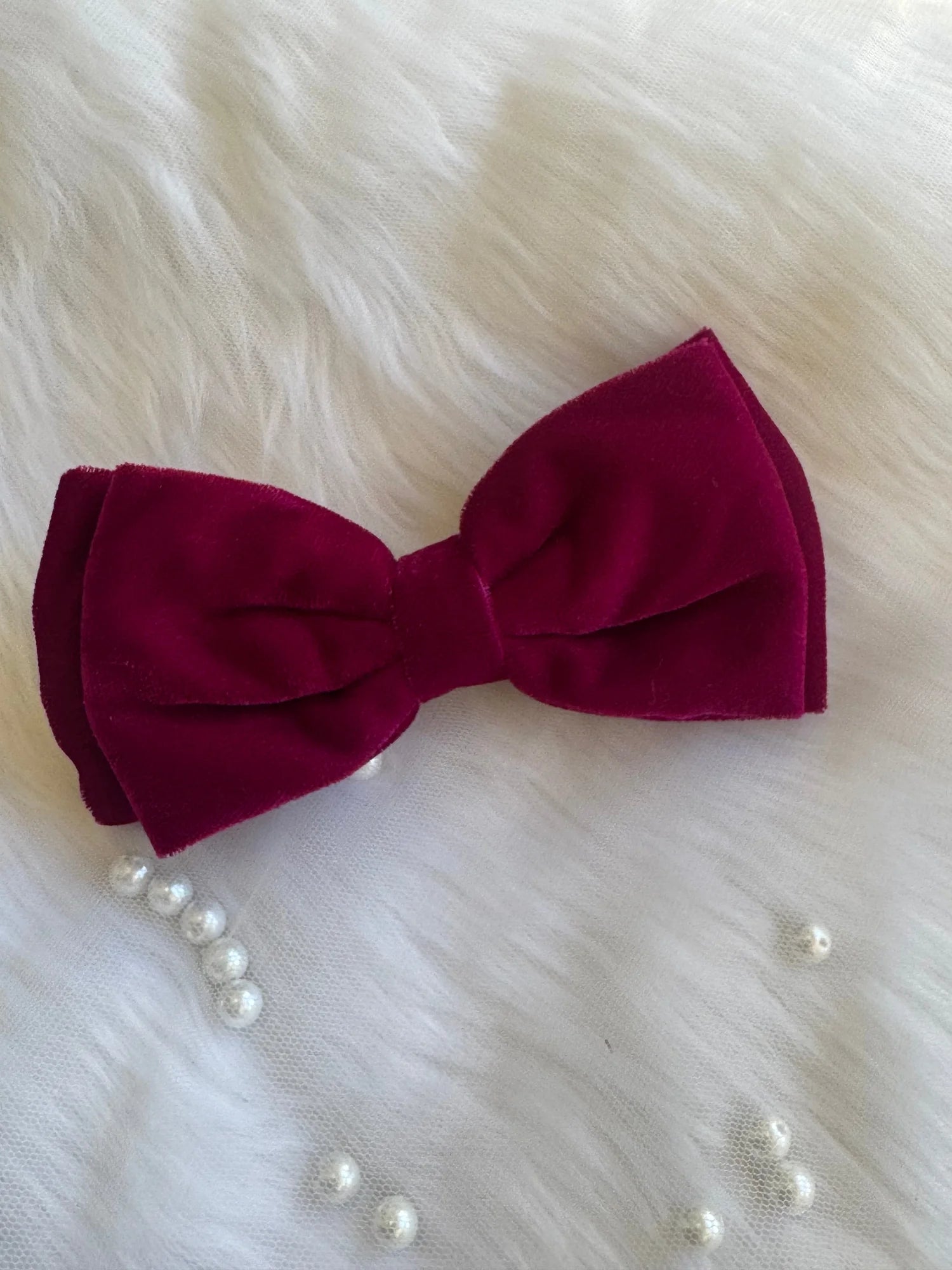 Magenta pink velvet hair bow by Bows and Bags India displayed with pearl beads on white fur, showing luxe texture and