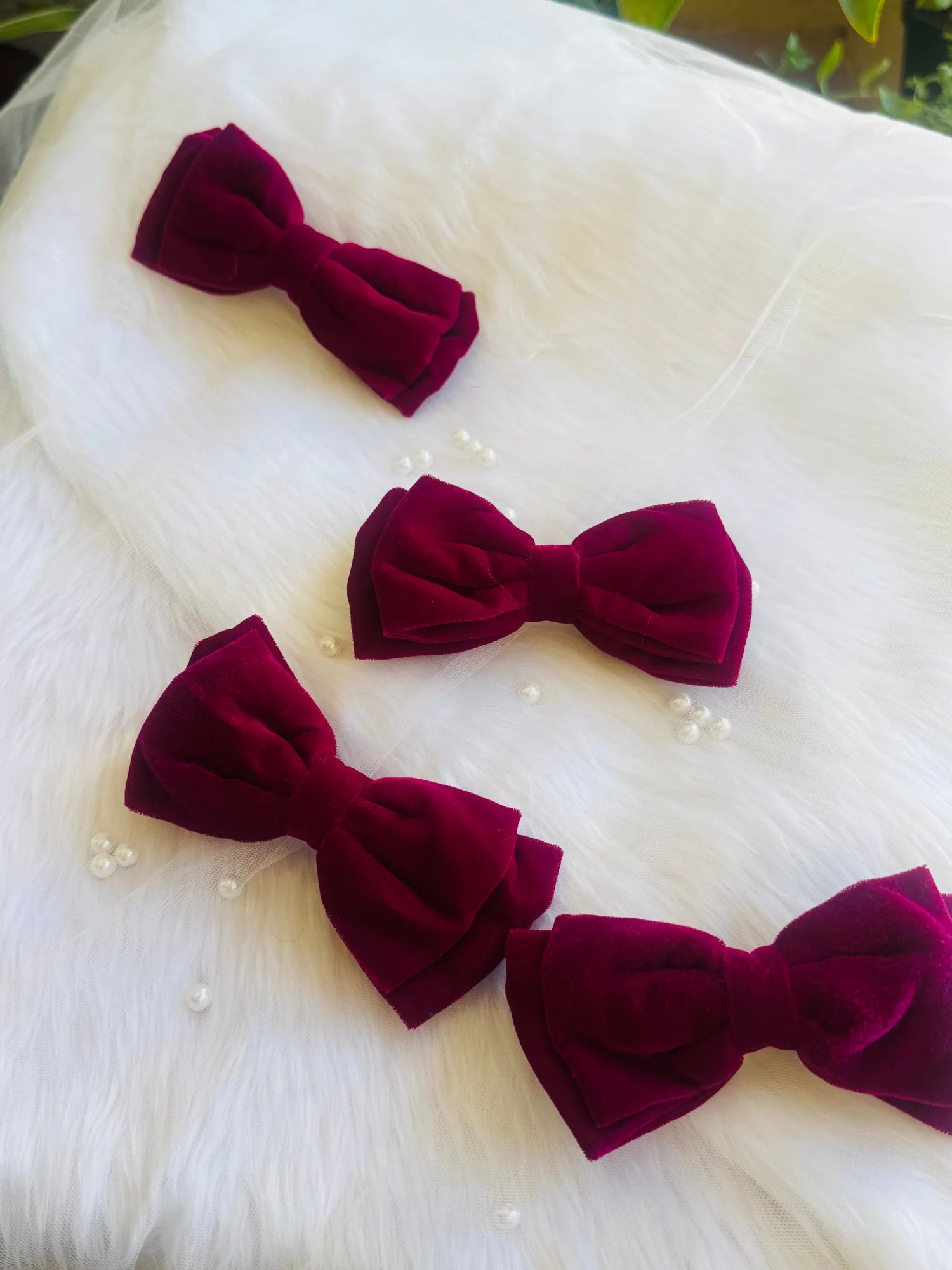 Four magenta velvet hair bows arranged on white fur, showcasing handmade bow designs by Bows and Bags India with luxurious