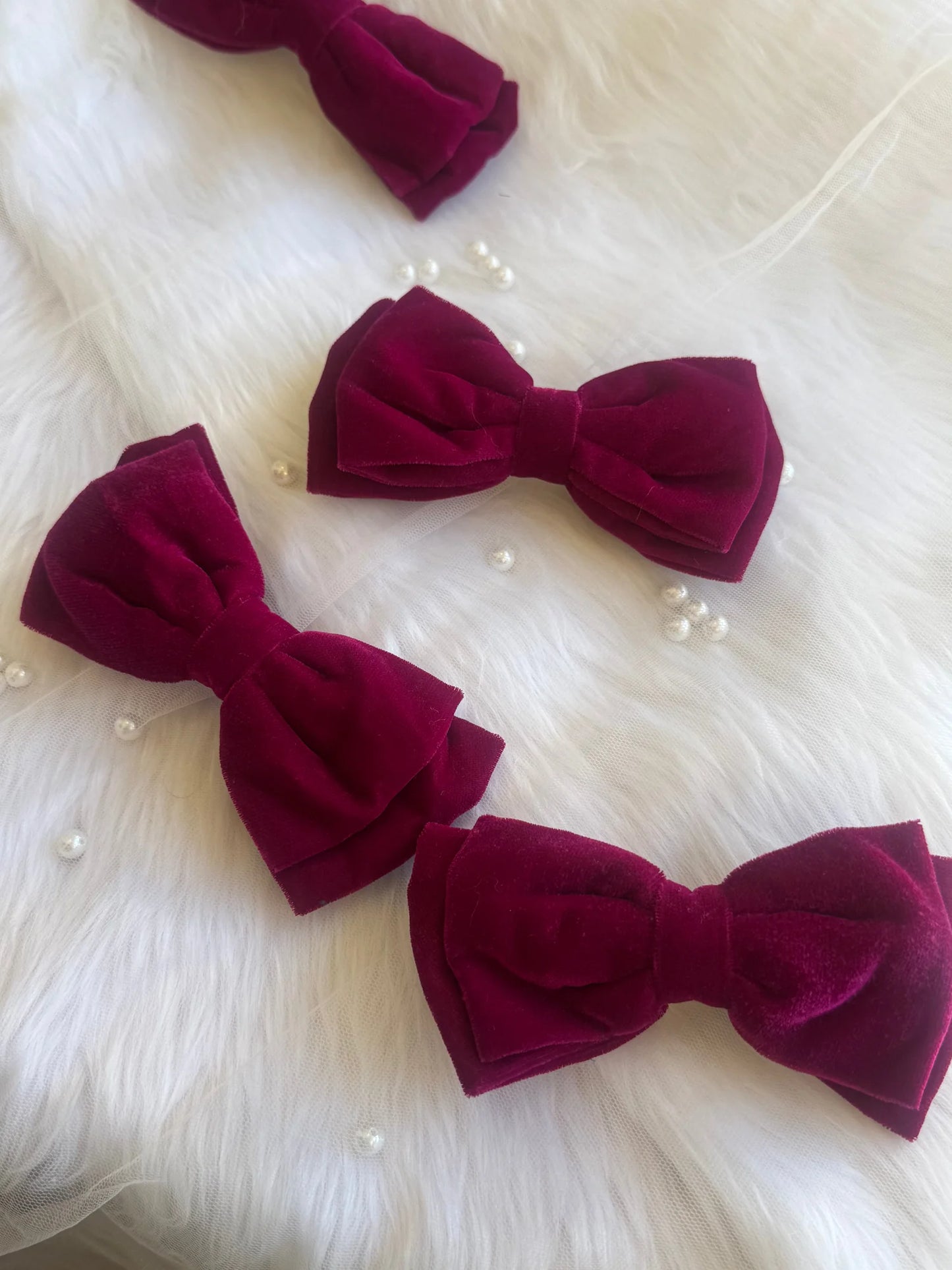 Three magenta velvet hair bows by Bows and Bags India arranged on white fur, displaying handmade premium texture and rich