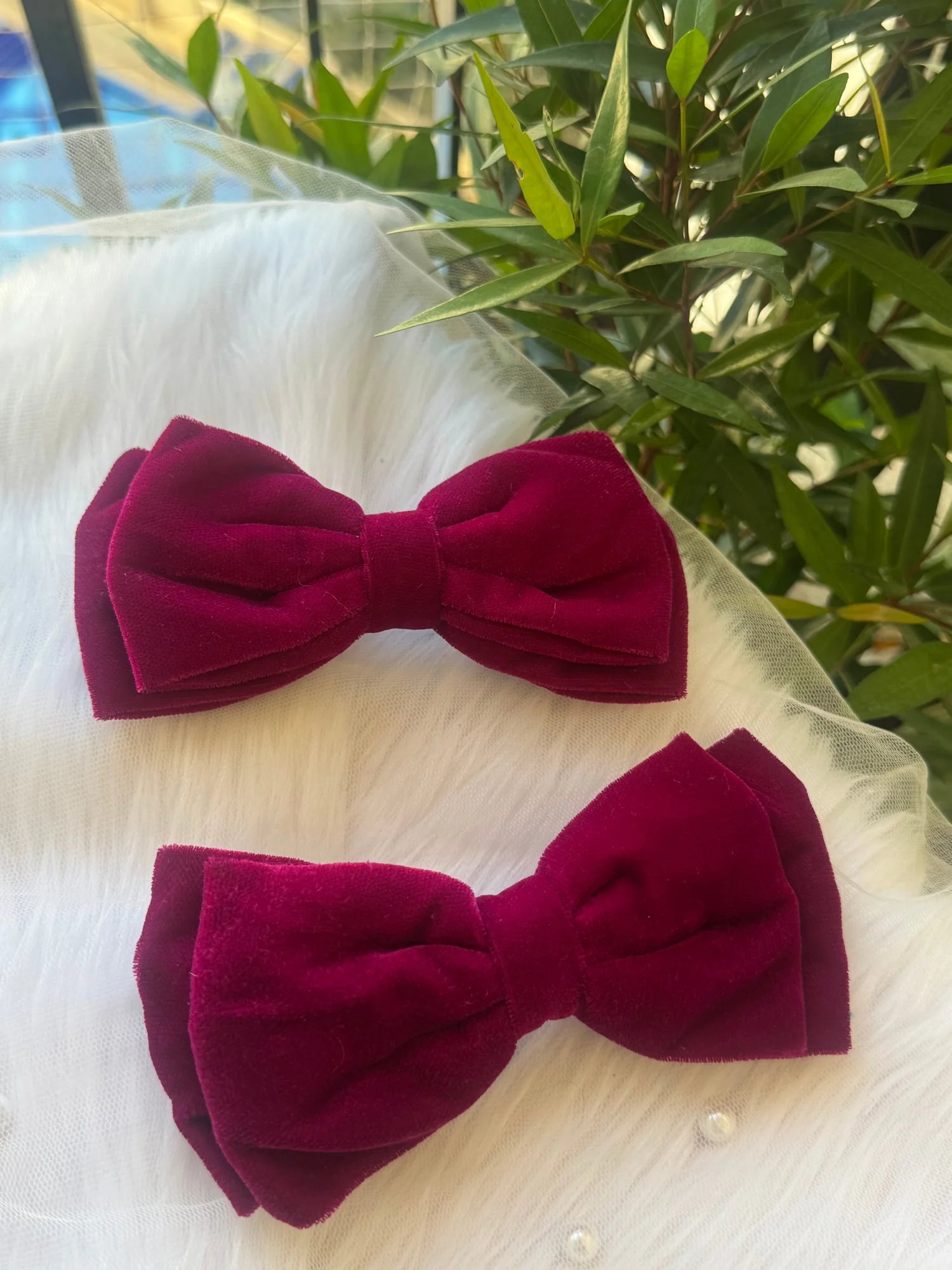 Two magenta velvet hair bows by Bows and Bags India displayed on white fabric with green plants, showing handmade premium