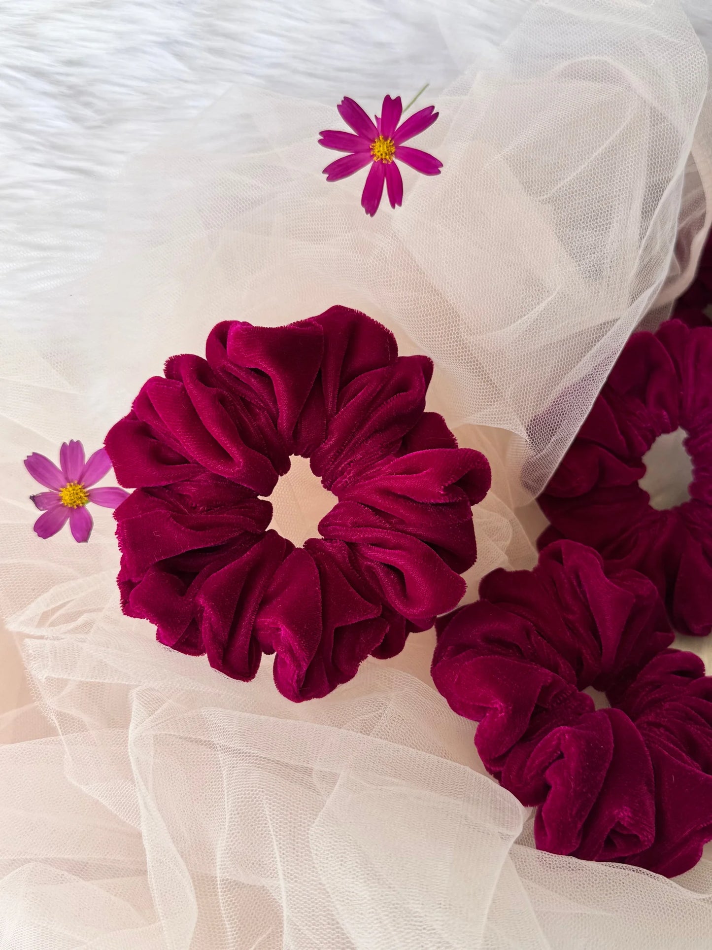 Hot pink velvet scrunchie by Bows and Bags India displayed on tulle with purple cosmos flowers, showing luxe texture and