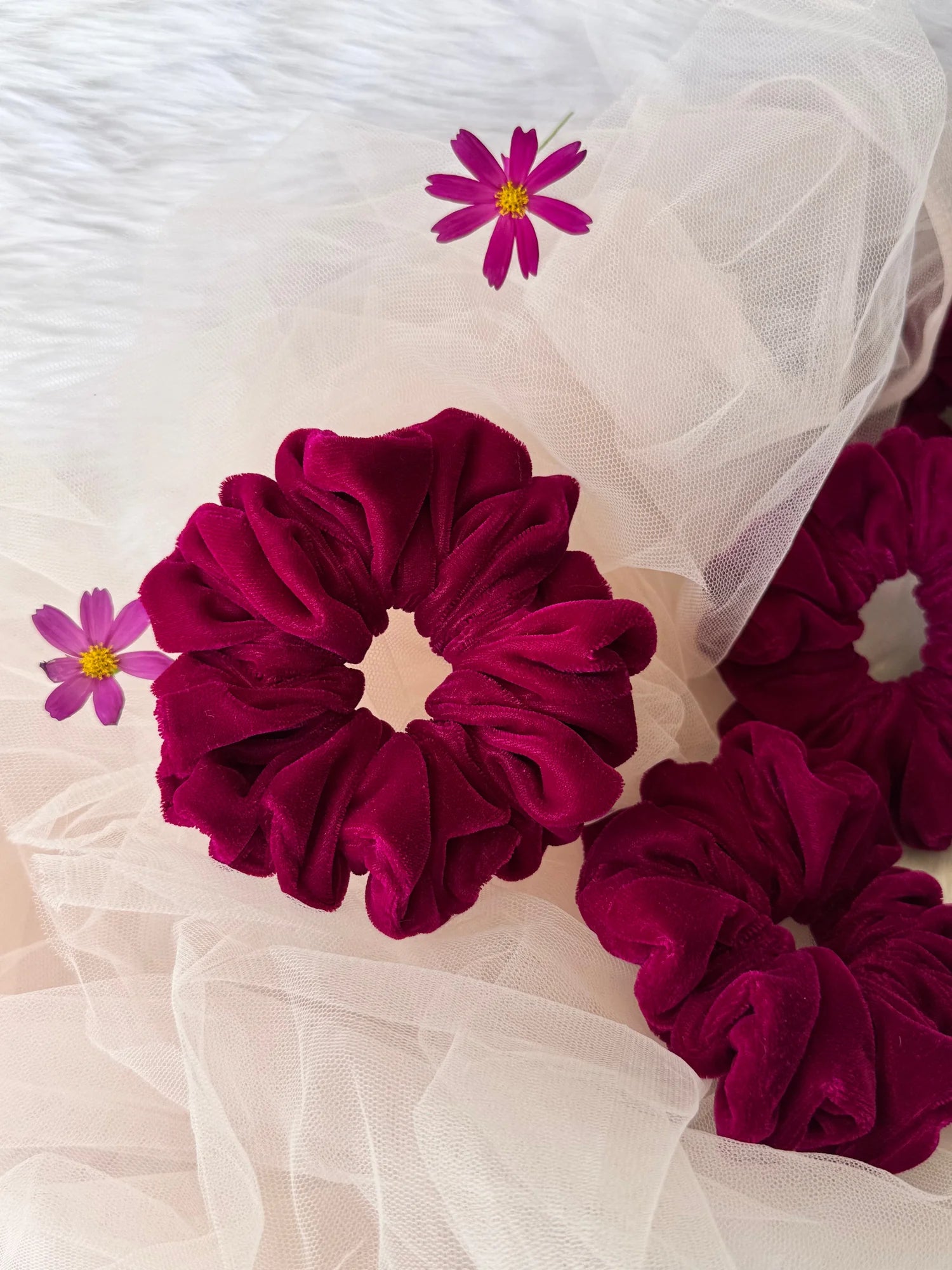 Hot pink velvet scrunchie by Bows and Bags India displayed on tulle with purple cosmos flowers, showing luxe texture and
