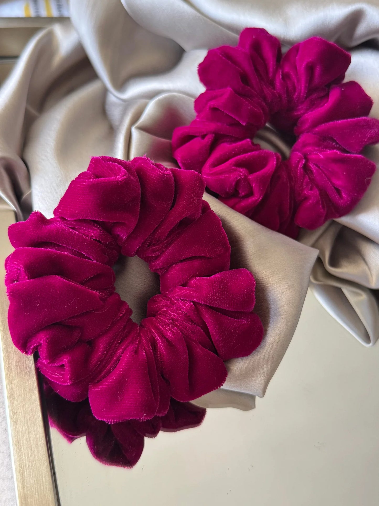 Hot pink luxe velvet scrunchie by Bows and Bags India displayed on cream fabric, showcasing rich texture and bold color of
