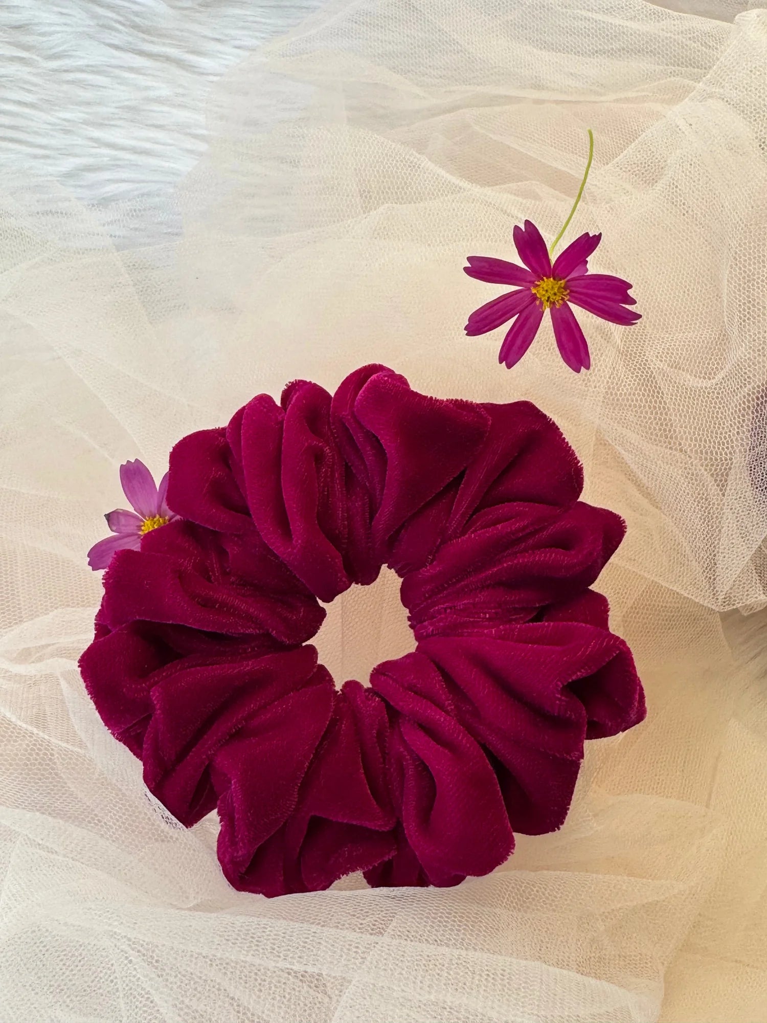 Hot pink velvet scrunchie by Bows and Bags India displayed with delicate flowers on cream fabric, showing luxe handmade hair