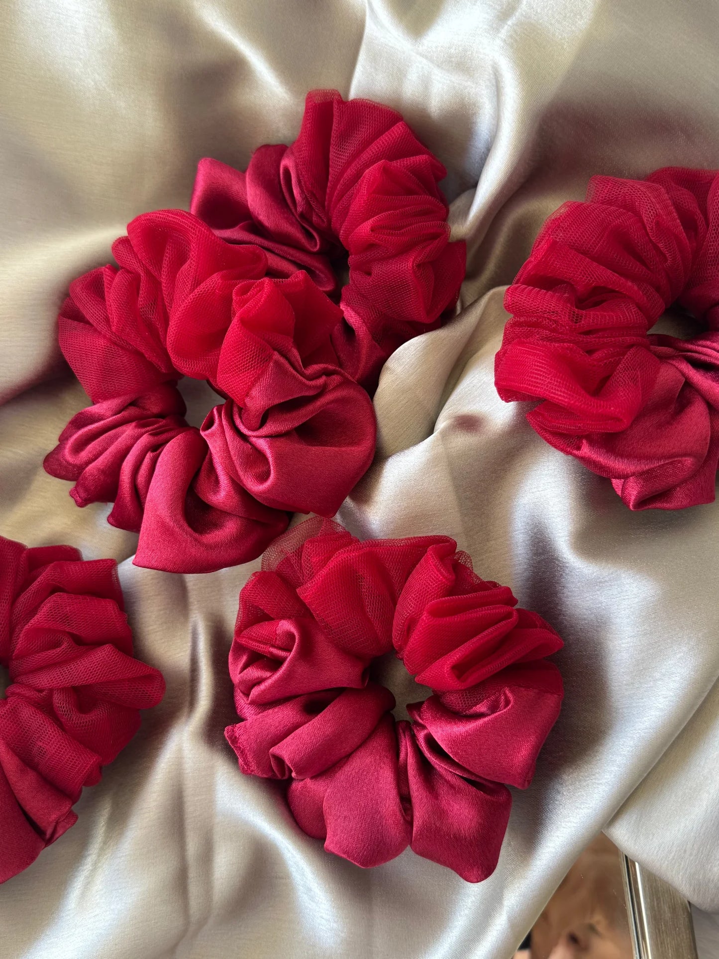 Crimson red satin scrunchies with net detailing arranged on cream fabric, handmade hair accessories by Bows and Bags India