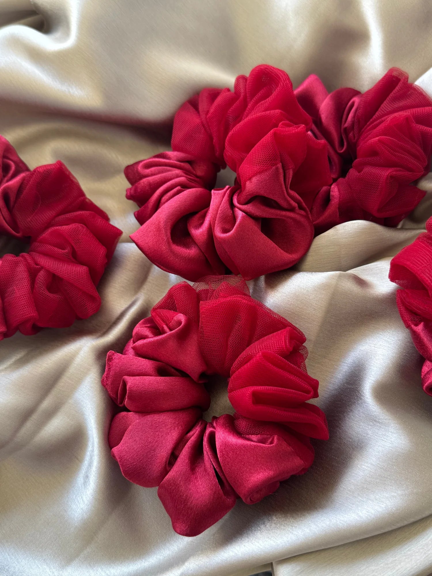 Crimson red satin scrunchies with net detailing arranged on cream fabric by Bows and Bags India handmade hair accessories