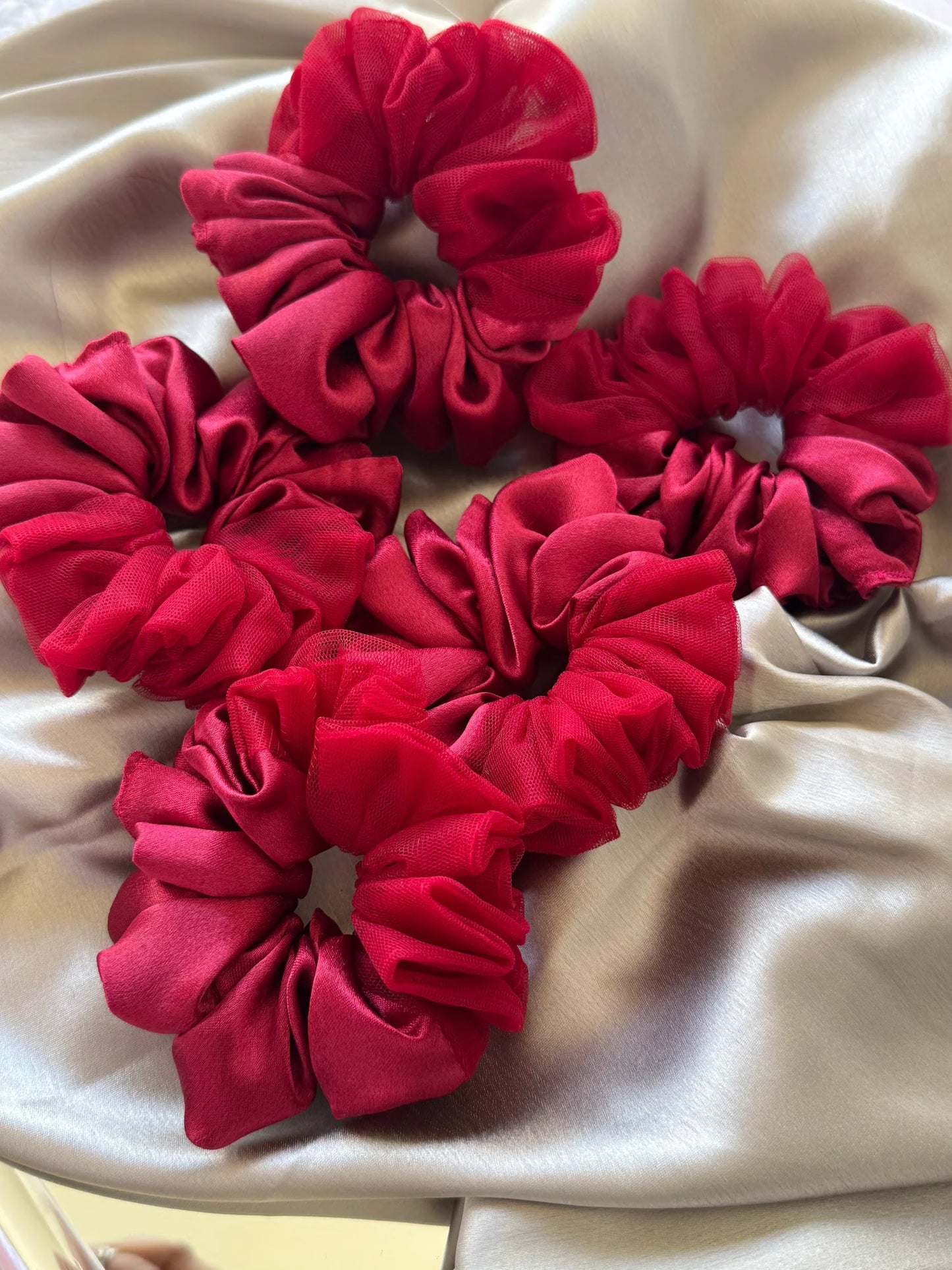 Crimson red satin scrunchies with net detailing arranged on cream fabric, handmade hair accessories by Bows and Bags India