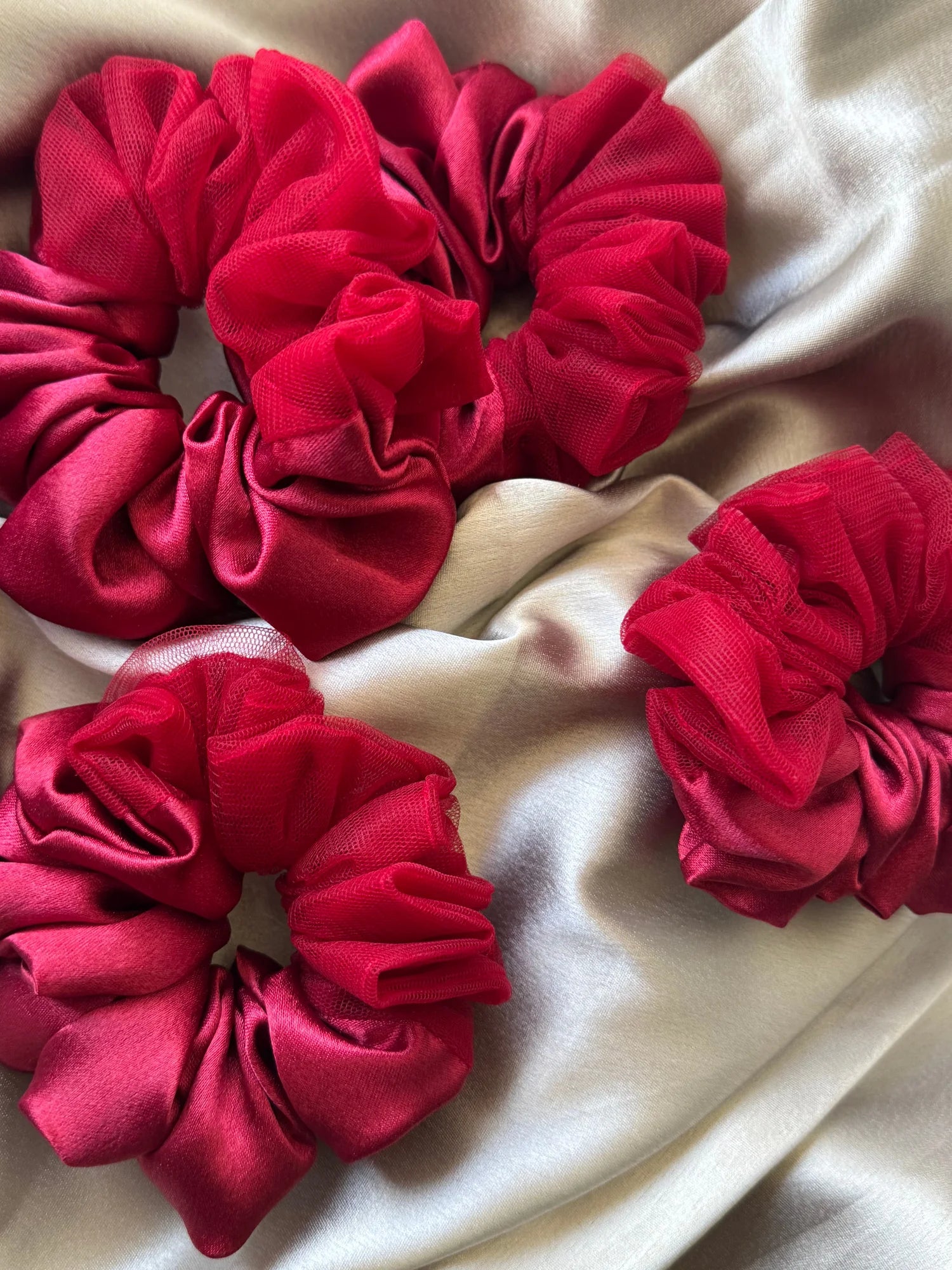 Crimson red satin scrunchies with net detailing arranged on cream fabric, handmade hair accessories by Bows and Bags India