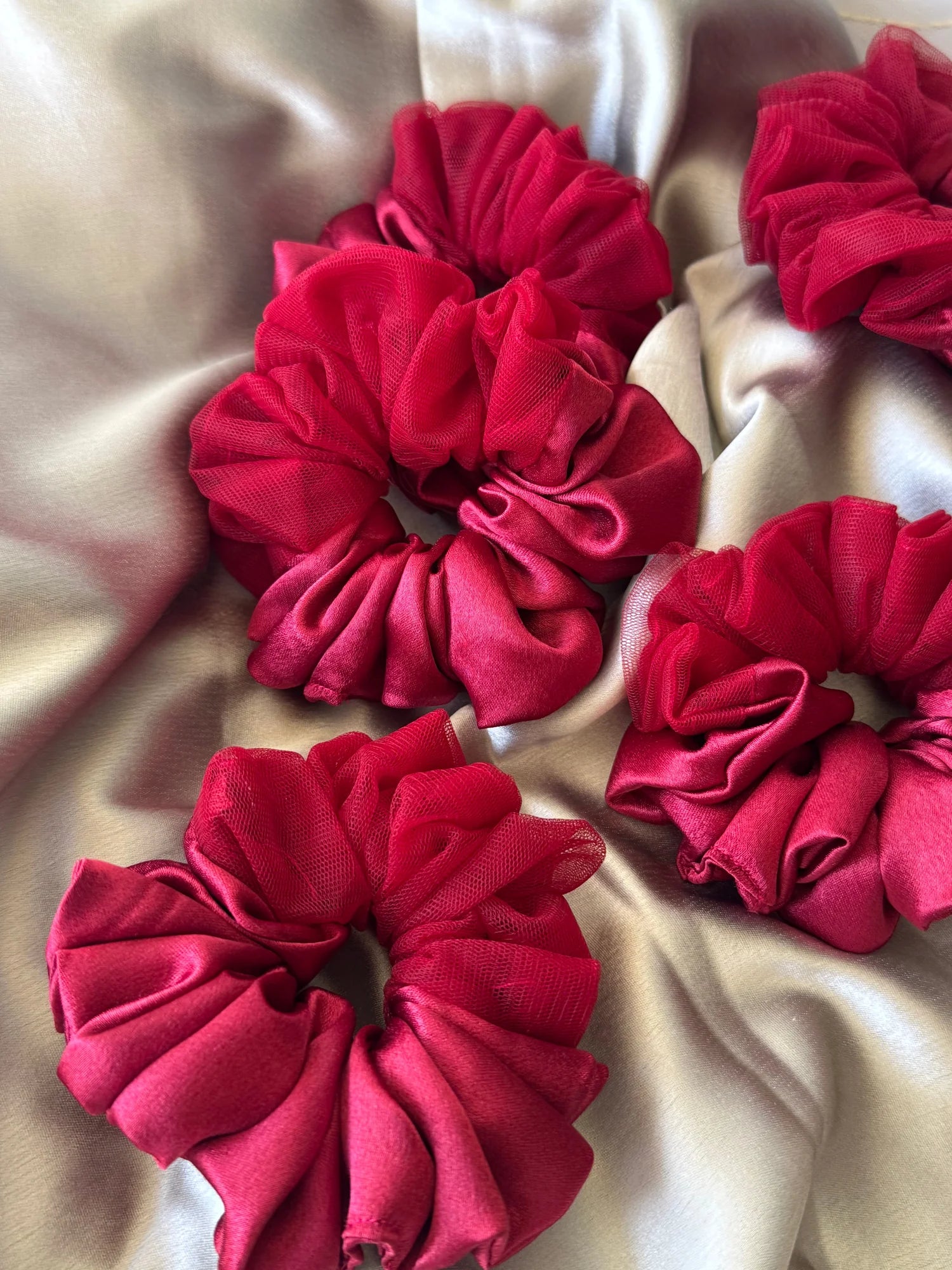 Crimson red satin scrunchies with net detailing displayed on cream fabric, showing handmade hair accessories from Bows and