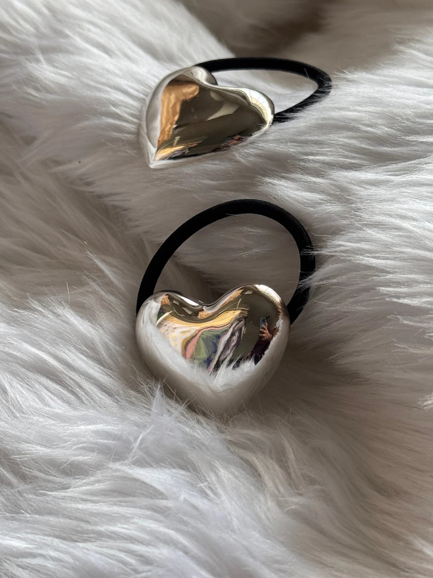 Two polished silver heart metal rubber bands with black elastic on white fur, showcasing Bows and Bags India handmade hair