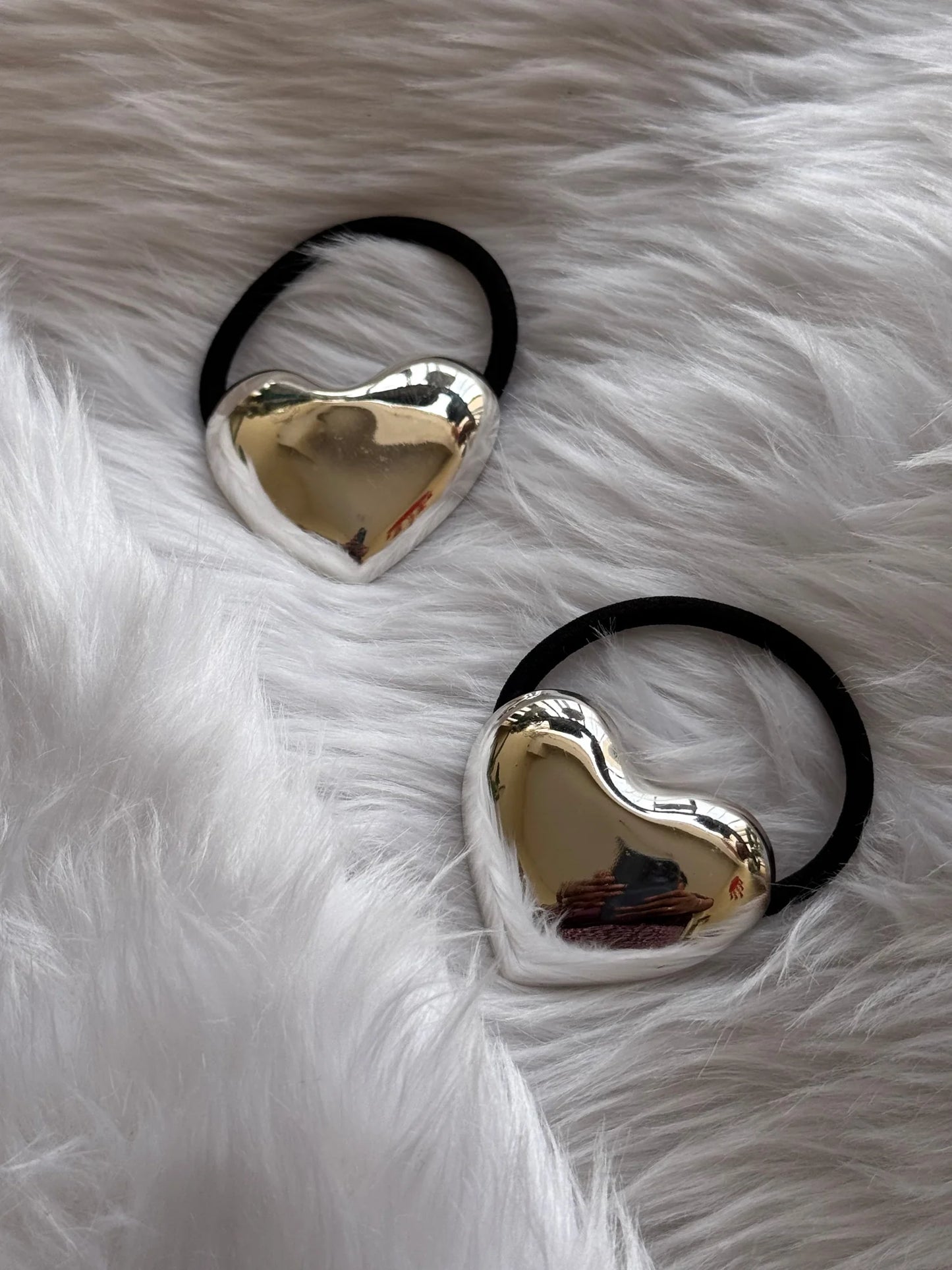 Two polished silver heart metal rubber bands with black elastic displayed on white fluffy fabric by Bows and Bags India
