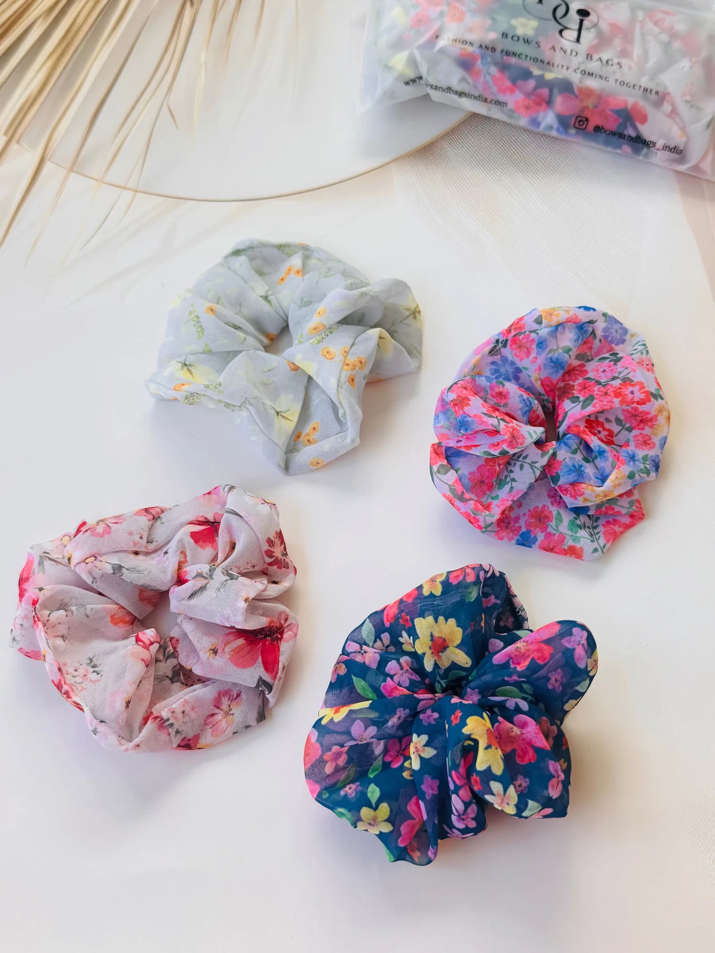 Four premium georgette scrunchies from Bows and Bags India in floral prints, flat lay styling on white surface
