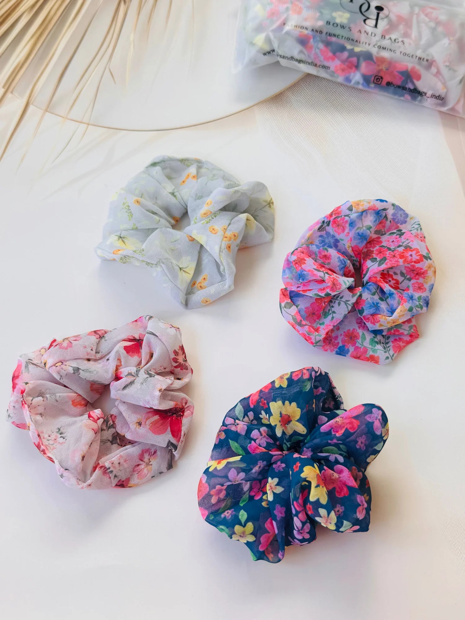 Four premium georgette scrunchies from Bows and Bags India in floral prints, flat lay styling on white surface