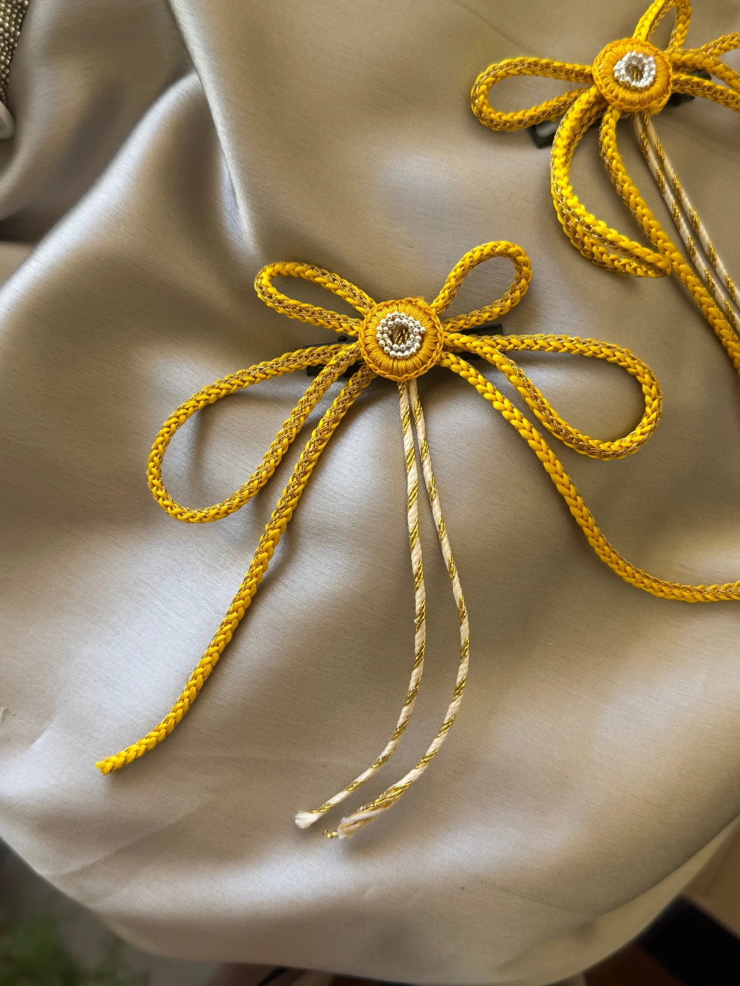 Golden rope bow hair clip with rhinestone center on cream fabric by Bows and Bags India