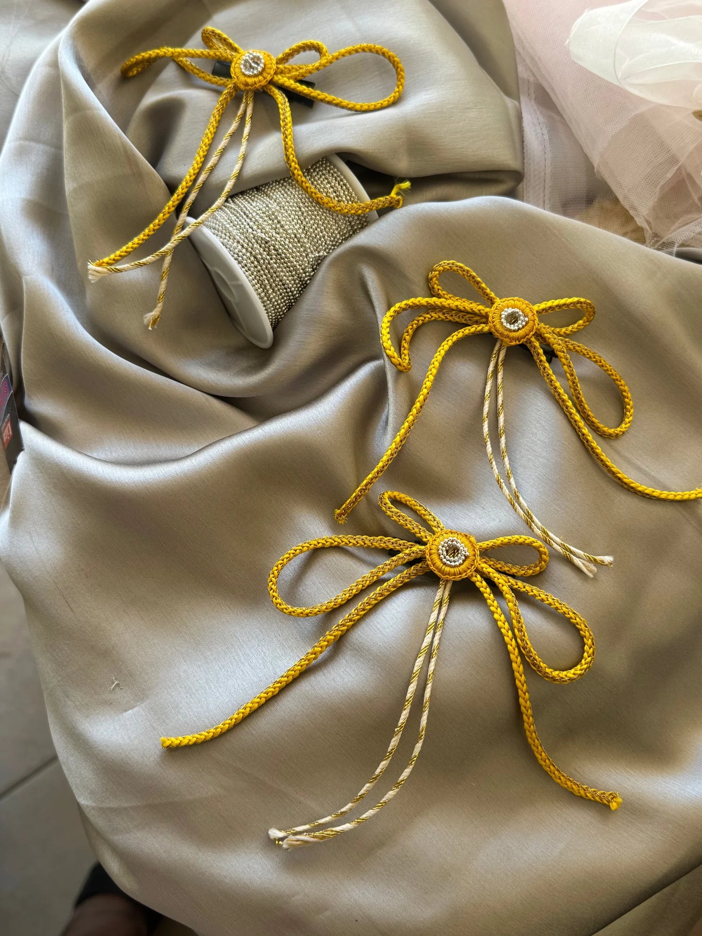 Handmade gold bow hair clips by Bows and Bags India displayed on cream fabric with beaded detail