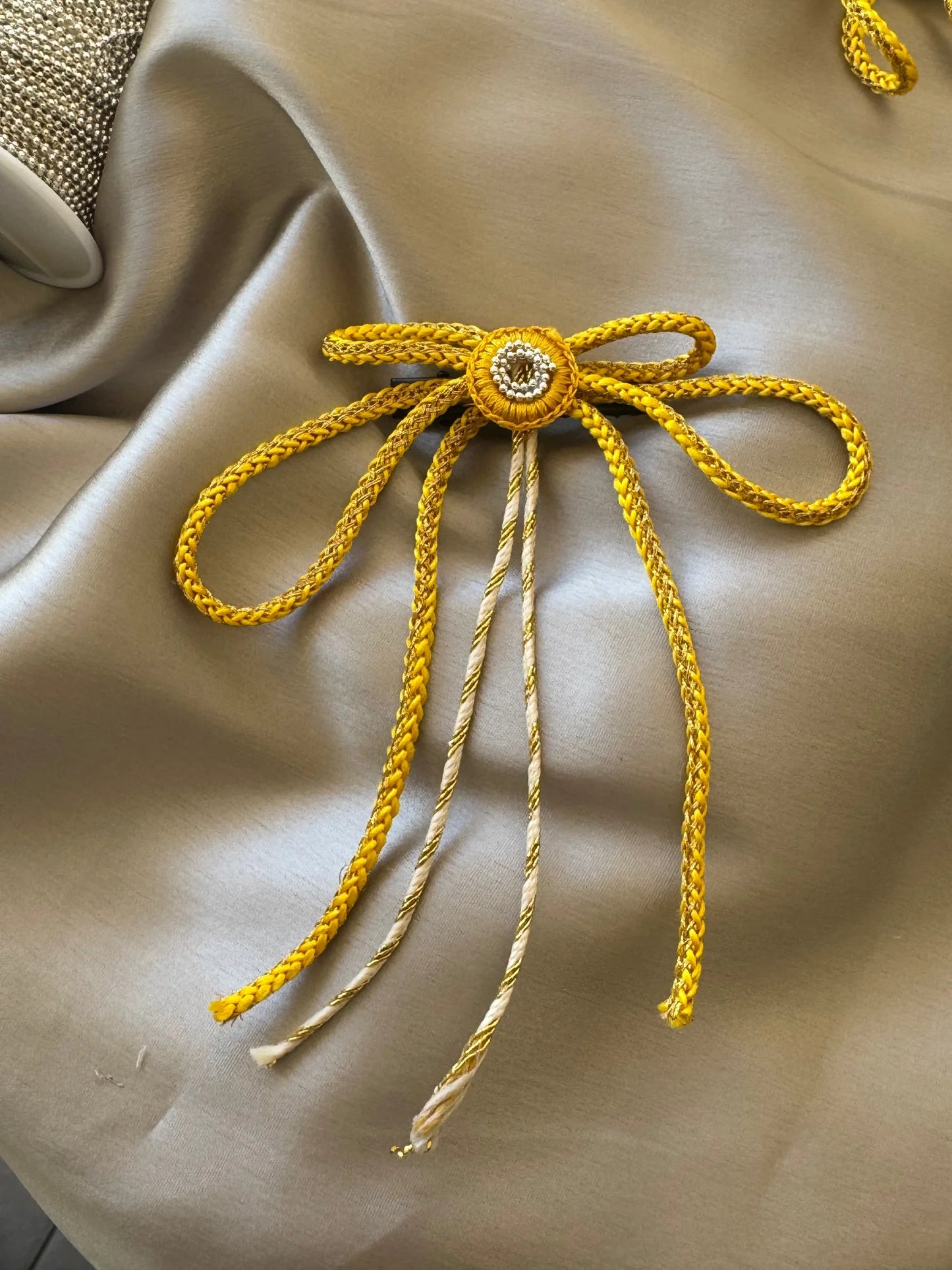 Handmade gold bow hair clip by Bows and Bags India with intricate detailing on cream fabric backdrop