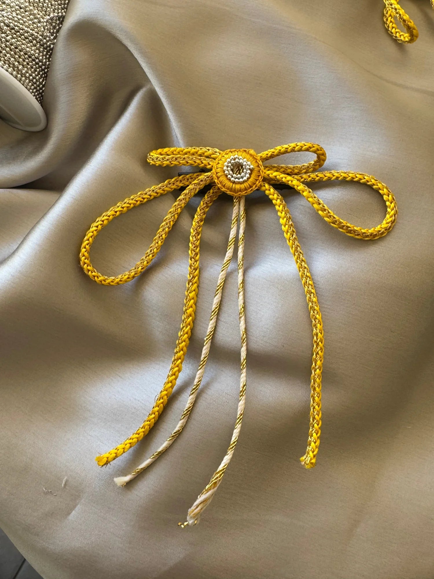 Handmade gold bow hair clip by Bows and Bags India with intricate detailing on cream fabric backdrop