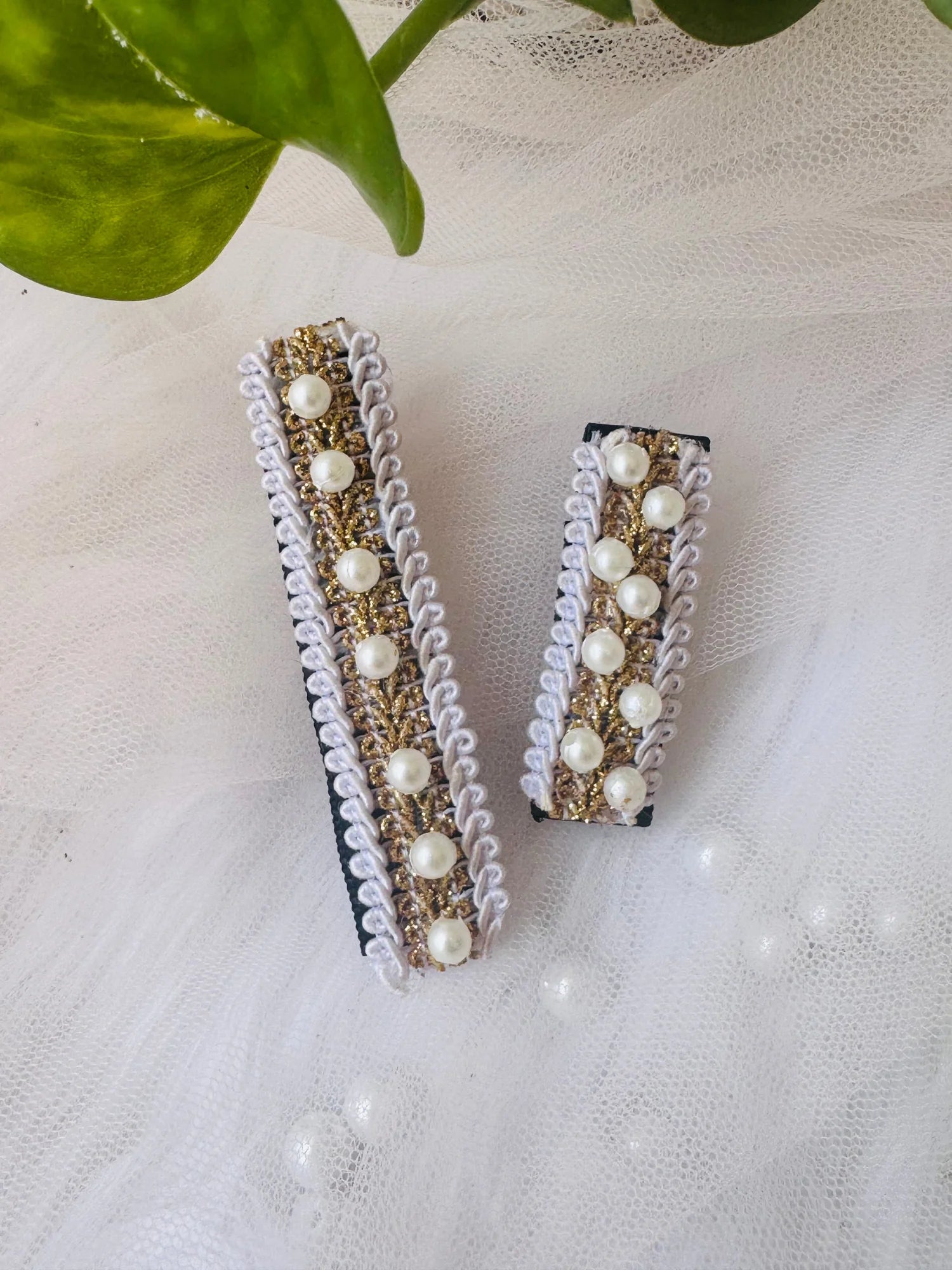 Pair of handmade pearl hair clips with gold glitter and white lace trim by Bows and Bags India, displayed on white textured