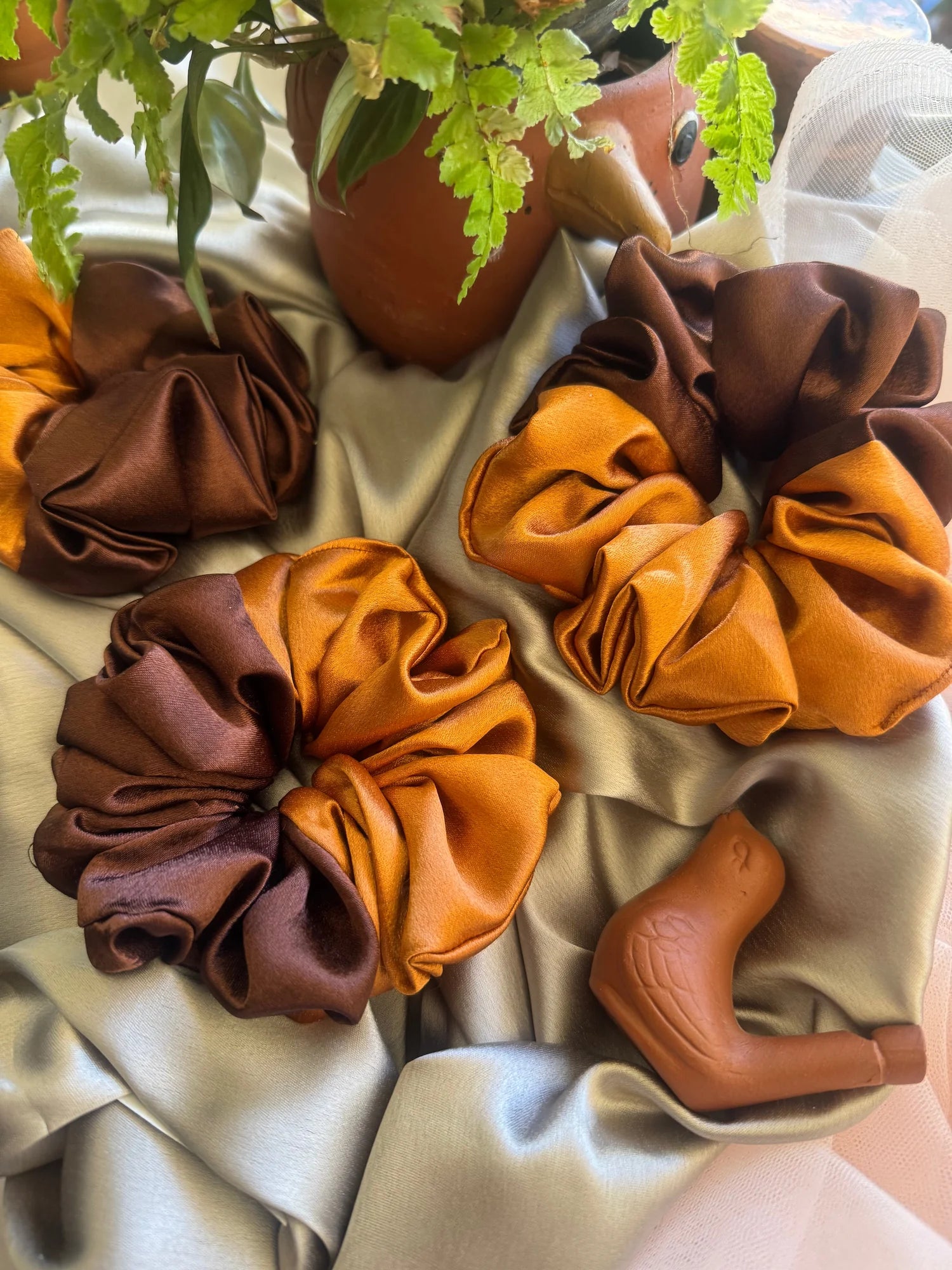 Terracotta and brown satin scrunchies by Bows and Bags India displayed on cream fabric with potted plant, showing handmade