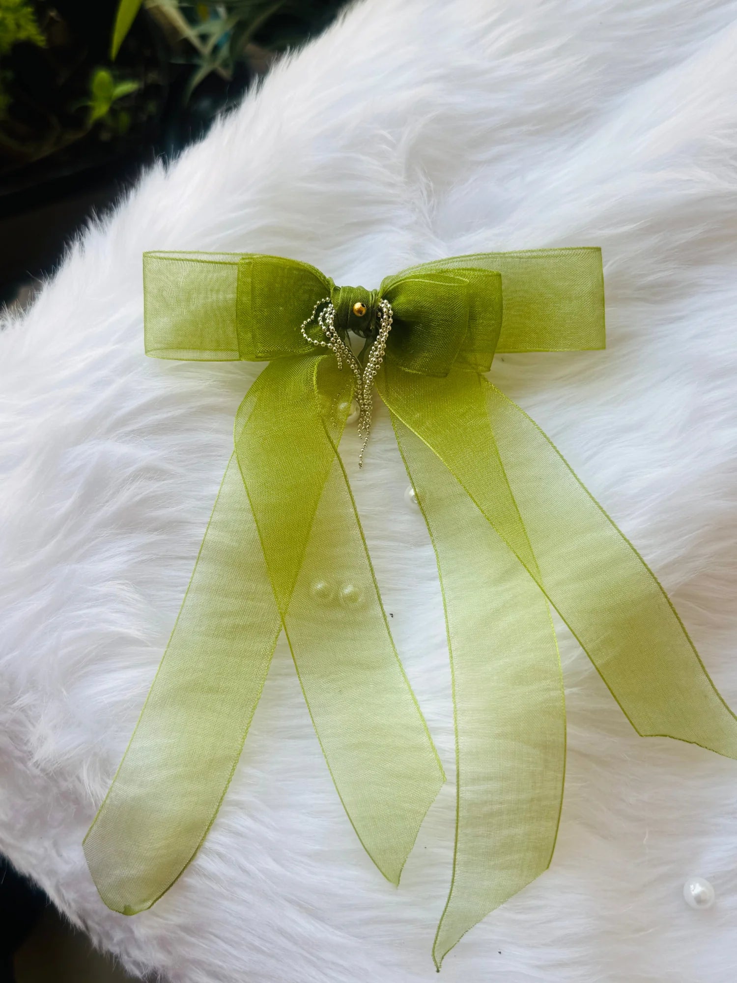Light green organza hair bow clip with silver chain detailing by Bows and Bags India, displayed on white fluffy fabric
