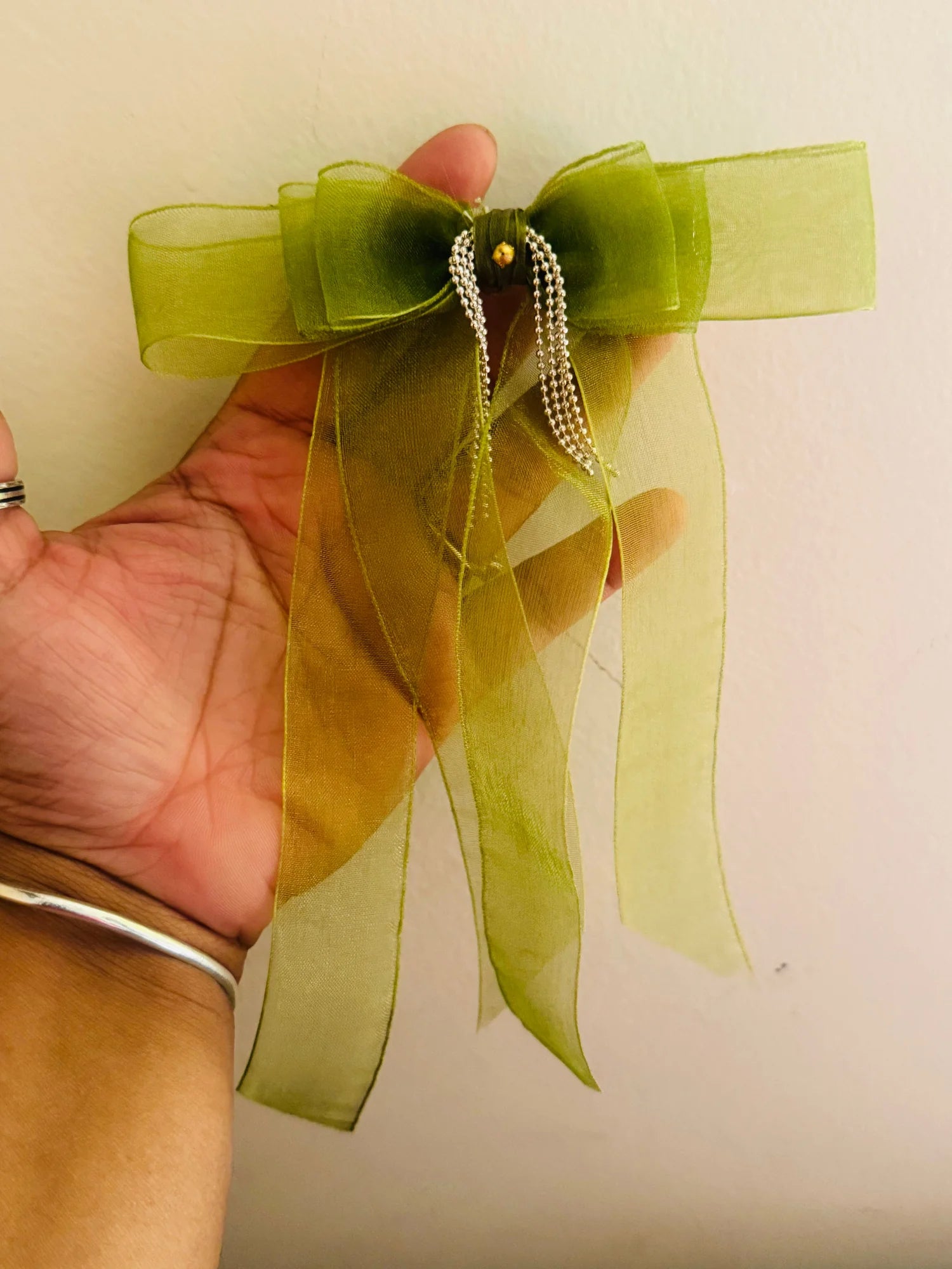 Handmade light green organza hair bow clip with delicate silver chain details held in hand, showcasing texture and elegance
