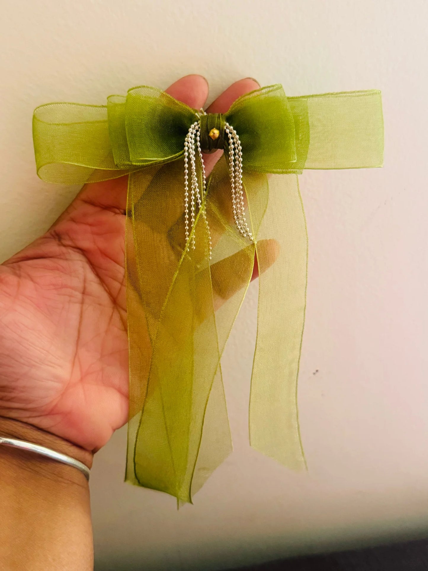 Light green organza hair bow clip with silver chain details held in hand, showcasing delicate handmade craftsmanship by Bows